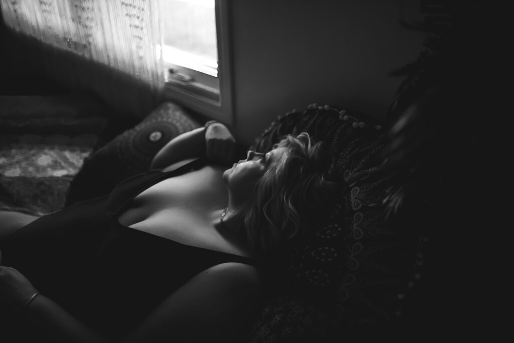 black and white boudoir photo of a woman gazing out the window while reclining in bed